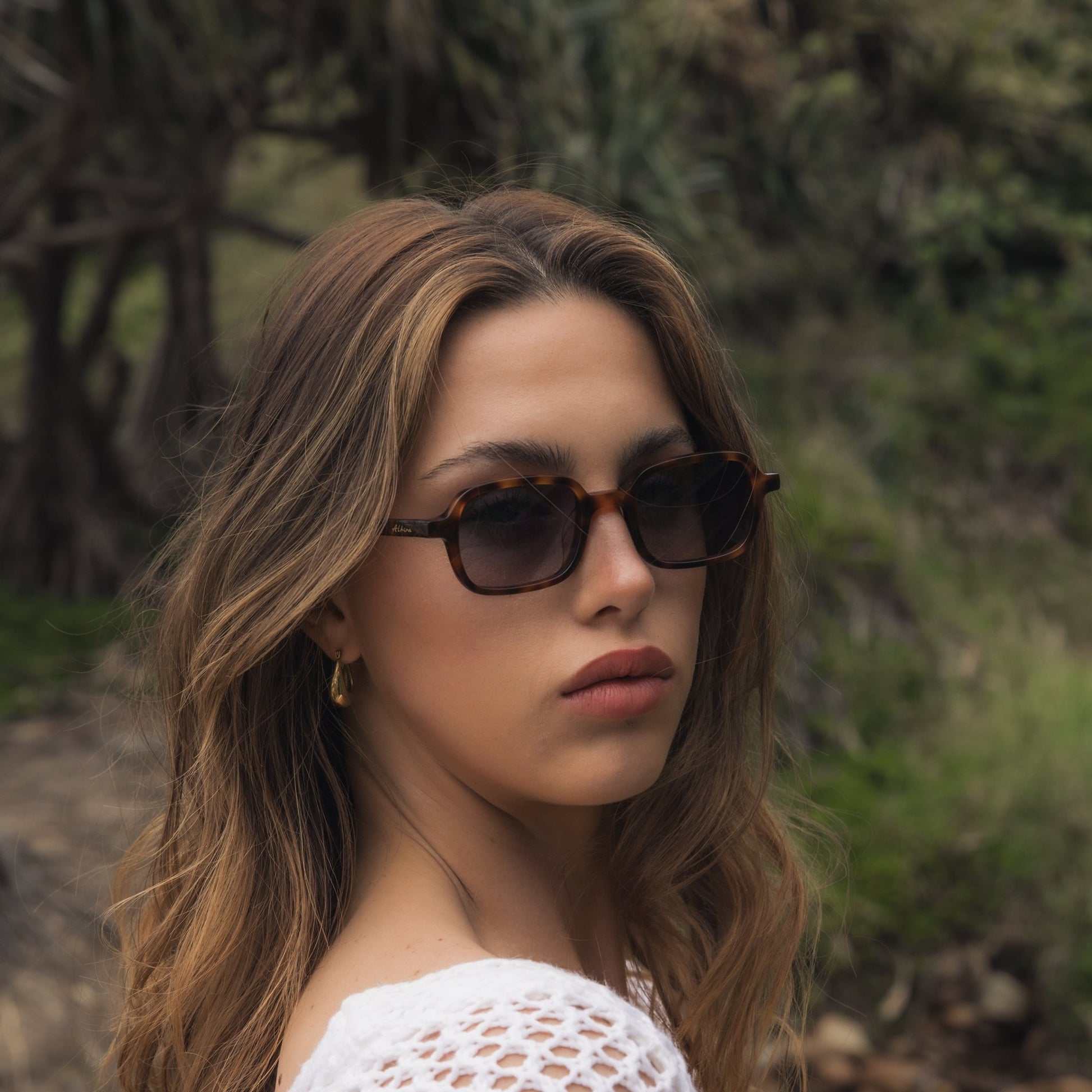 Woman wearing Alkira branded sunglasses and a white crochet top outdoors