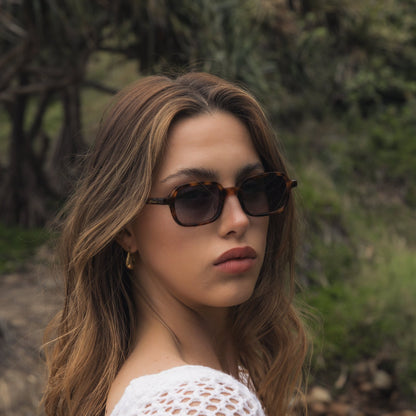 Woman wearing Alkira branded sunglasses and a white crochet top outdoors