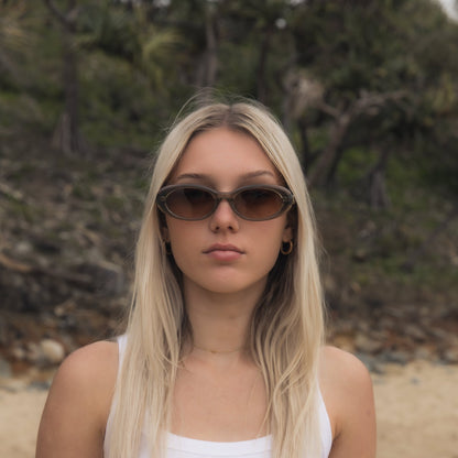 Woman wearing Alkira branded sunglasses and a white top on a beach