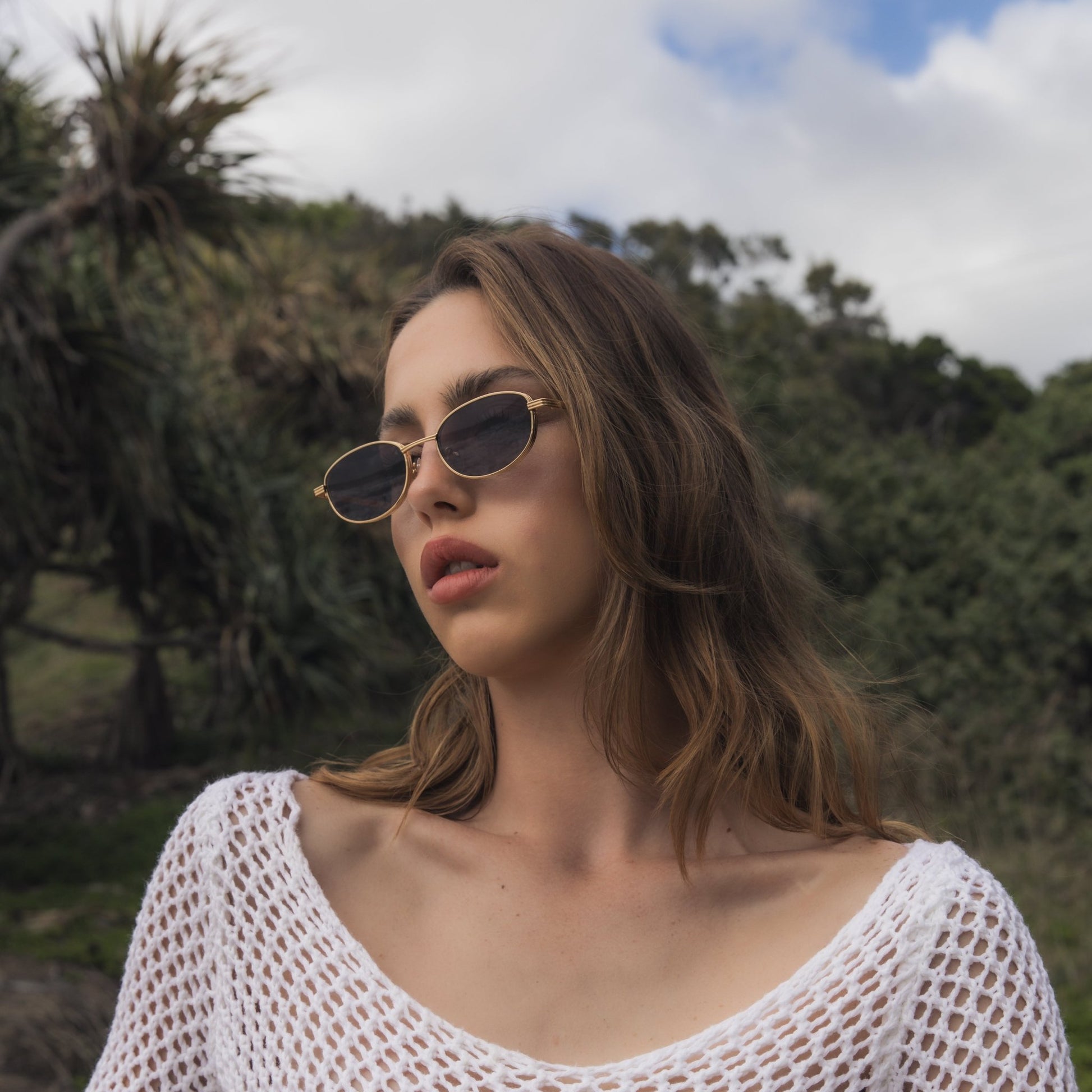 Woman wearing a white crochet top with a blurred natural background